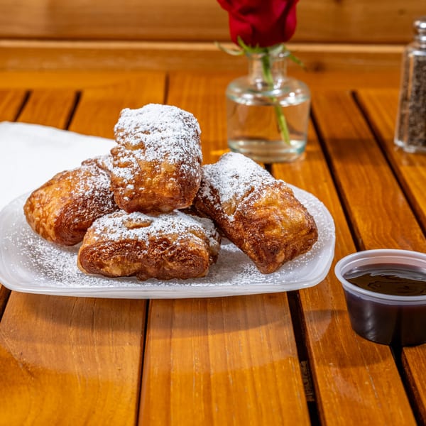 Chloez Cafe's beignets, dusted with powdered sugar, served with dipping sauce on a wooden table.