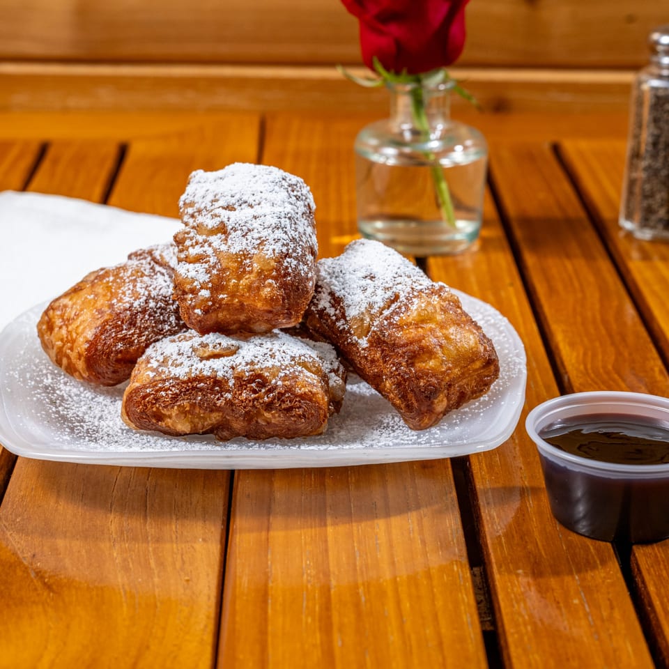 Chloez Cafe's beignets, dusted with powdered sugar, served with dipping sauce on a wooden table.