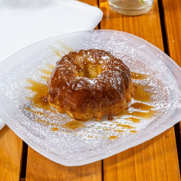 A golden bundt cake drizzled with caramel and powdered sugar on a white plate.