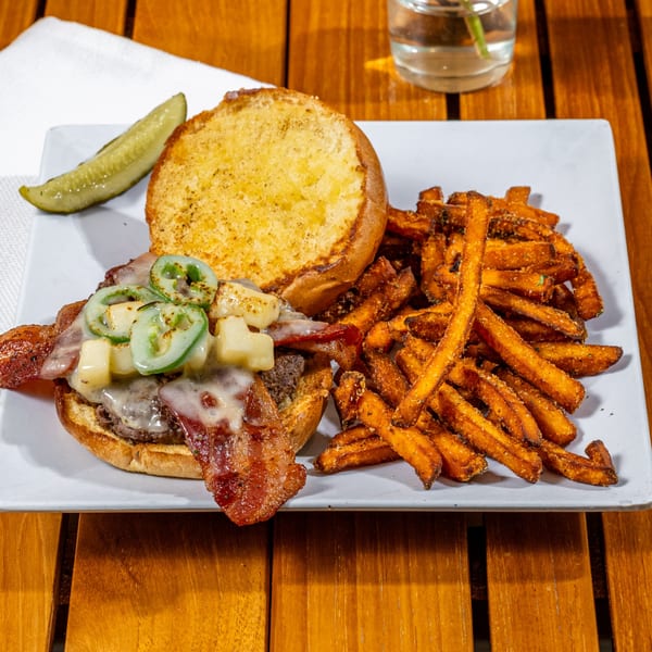 Chloez Cafe's bacon cheeseburger with jalapeños, pineapple, and sweet potato fries on a white plate.